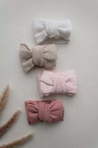 Knitted baby bow headbands in beige, light pink and dusty pink, arranged together to show the different colour options.