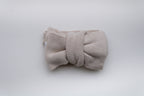 Beige knitted baby bow headband with a matching fabric bow, displayed on a light neutral background.