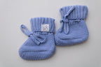 Blue knitted baby booties for newborns, featuring textured knit, ribbed cuffs, knitted ties and Snuggle Threads label.