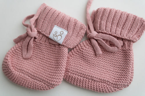 Close-up of dusty pink knitted newborn baby booties with textured stitching, ribbed cuffs, tie closures and Snuggle Threads label.