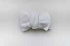 Ivory knitted baby bow headband with a matching knitted bow, displayed on a light neutral background.