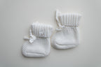 Close-up of ivory knitted baby booties with soft textured knit, ribbed cuffs, tie closures and Snuggle Threads woven label.