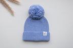 Blue knitted newborn baby hat with a matching fluffy pom pom, ribbed folded brim and Snuggle Threads woven label.