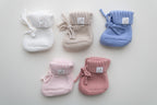 Knitted newborn baby booties in five colours: ivory, beige, blue, light pink and dusty pink, featuring ribbed cuffs and tie closures.
