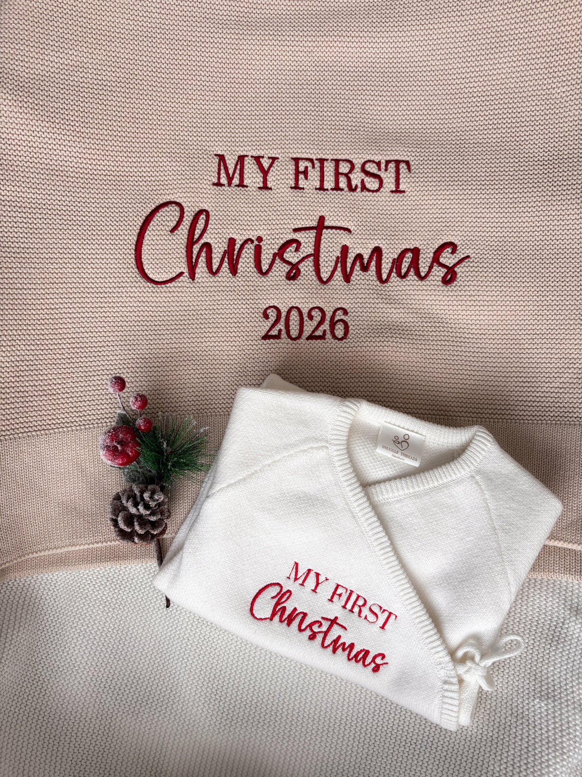 Ivory knitted baby wrap romper with red My First Christmas embroidery, displayed on a matching personalised Christmas baby blanket with 2026 design.