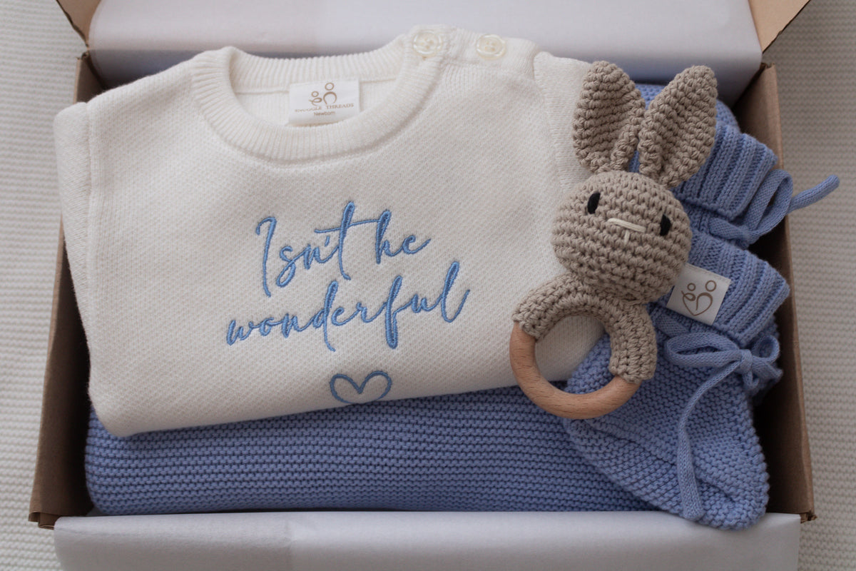 Personalised baby gift box with ivory embroidered romper, blue knitted blanket and booties, and crochet bunny rattle