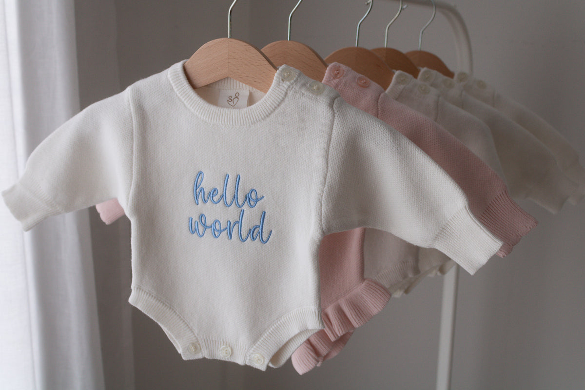 Personalised knitted baby rompers in ivory and pink hanging on wooden hangers