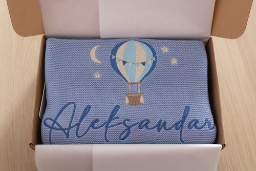 Personalised blue knitted baby blanket with hot air balloon embroidery and the name Aleksandar presented in a gift box