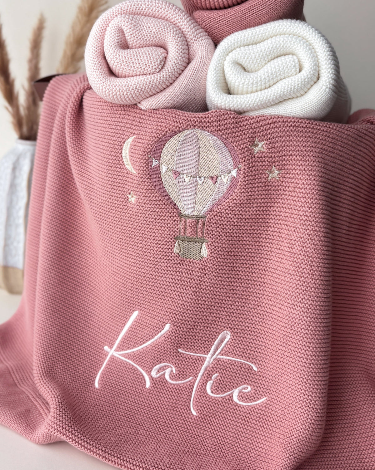 Personalised dusty pink knitted baby blanket with hot air balloon embroidery and the name Katie