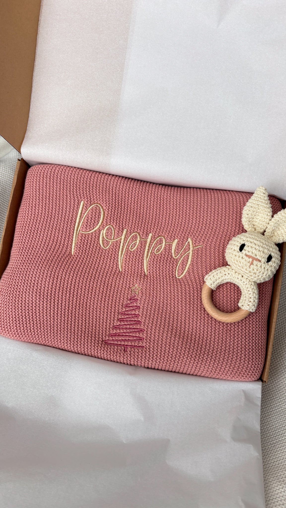 Personalised dusty pink knitted baby blanket with embroidered name and Christmas tree design, presented in a gift box with white tissue paper