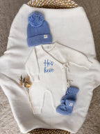 Personalised He's Here baby wrap romper with blue knitted hat and baby booties