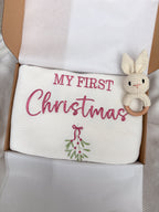 White knitted baby blanket personalised with pink My First Christmas embroidery and mistletoe, presented in a gift box with a crochet bunny rattle.