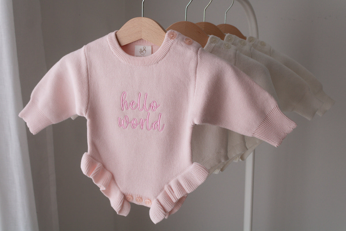 Pink knitted baby romper available for personalised embroidery hanging on a wooden hanger